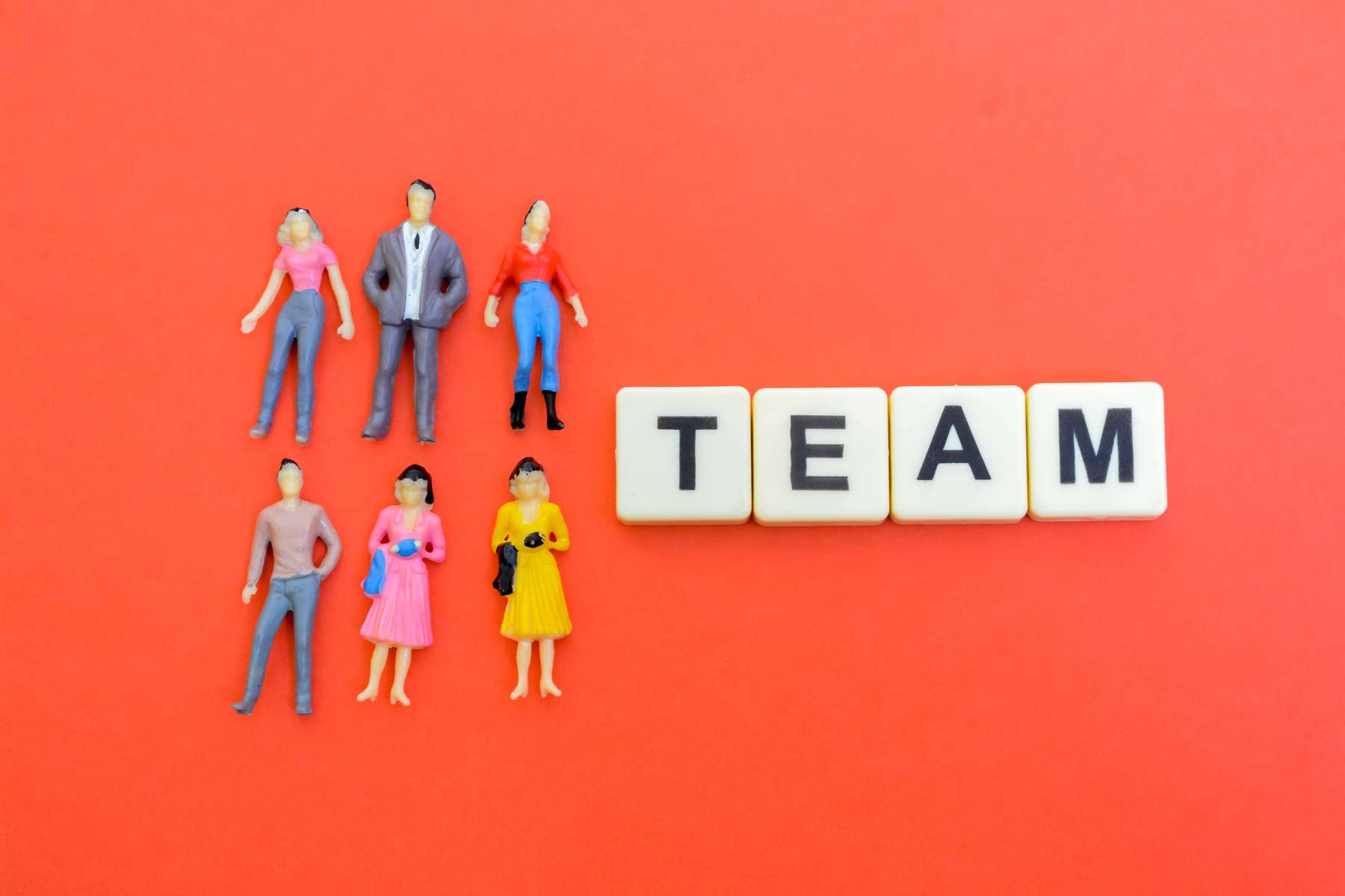 Auf rotem Untergrund liegen 6 männliche und weibliche Figürchen neben 4 Spielsteinen, die das Wort Team bilden.