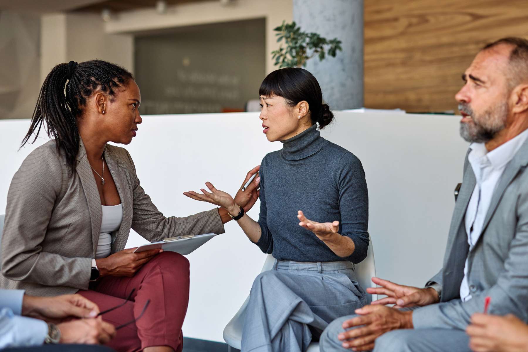 Eine Gruppe diverser Angestellter sitzt in einem Sitzkreis und diskutiert mit kritischen Gesichtsausdrücken.