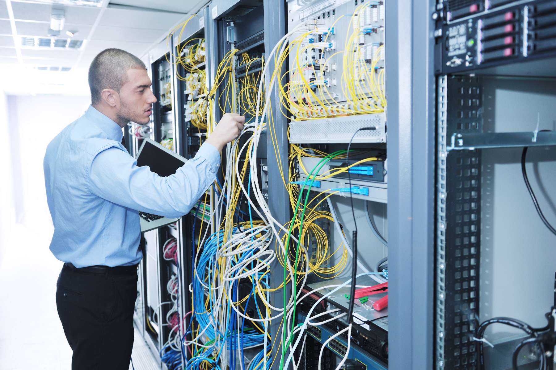 Ein Mitarbeiter der IT steht vor einem großen Serverschrank und kümmert sich um die Verkabelung.