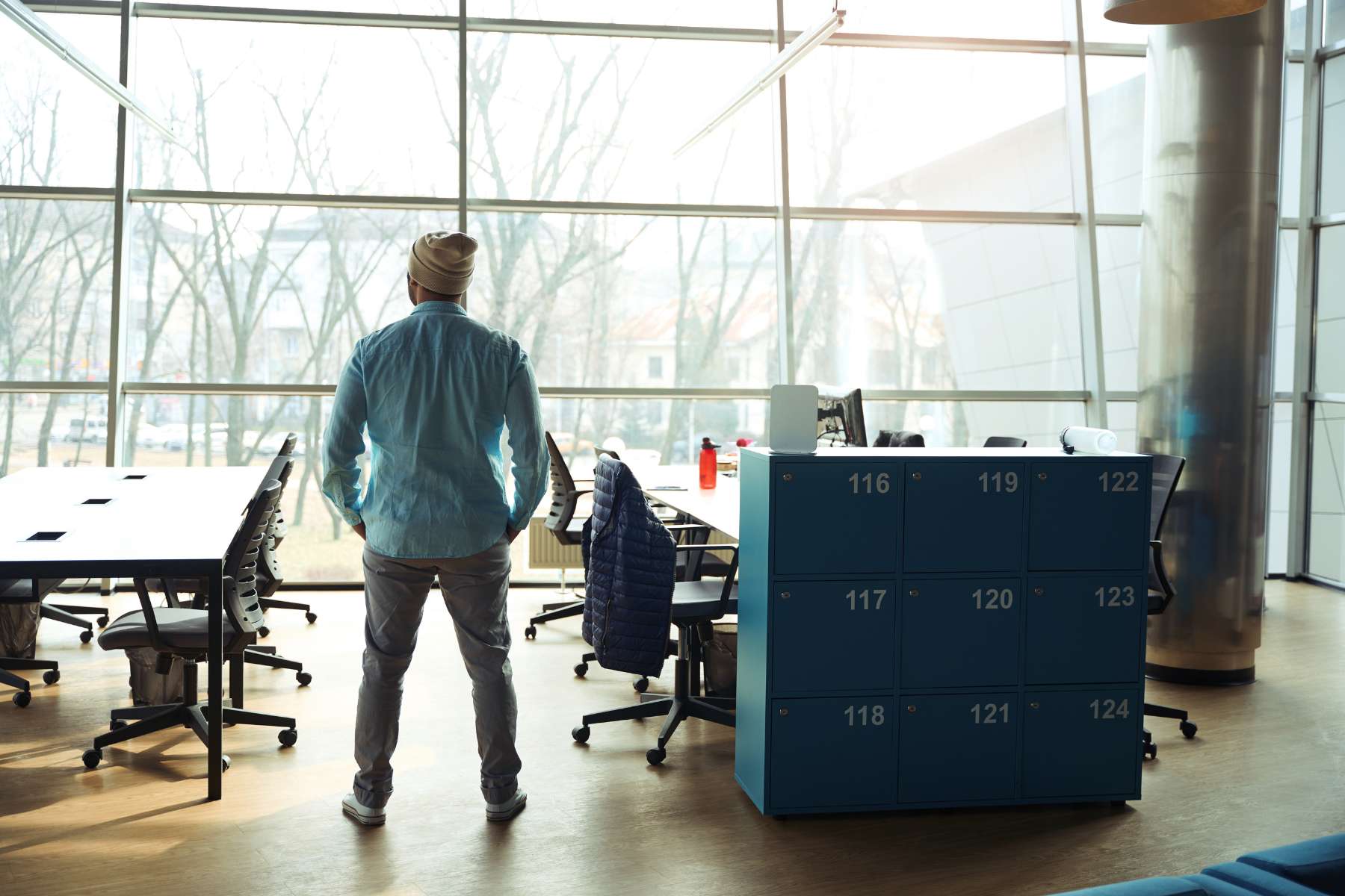 Ein männlicher Angestellter steht in einem großen Büro, in dem er alleine arbeitet, und schaut aus dem Fenster, als Sinnbild für Einsamkeit im Job.