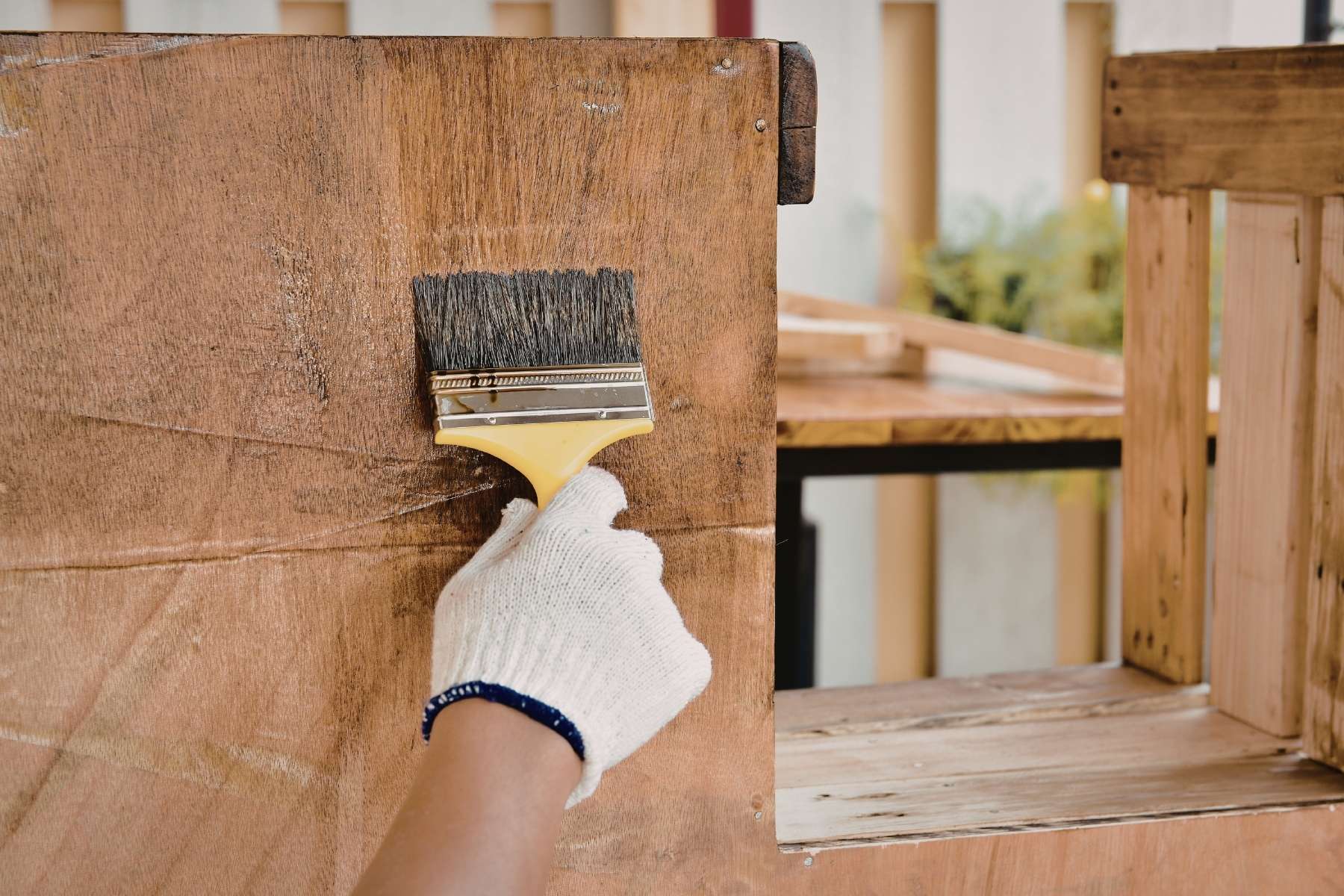 Nahaufnahme einer behandschuhten Hand die einen Pinsel in der Hand hält und ein Holzregal lasiert, als Sinnbild kreislaufförmiger Büros.