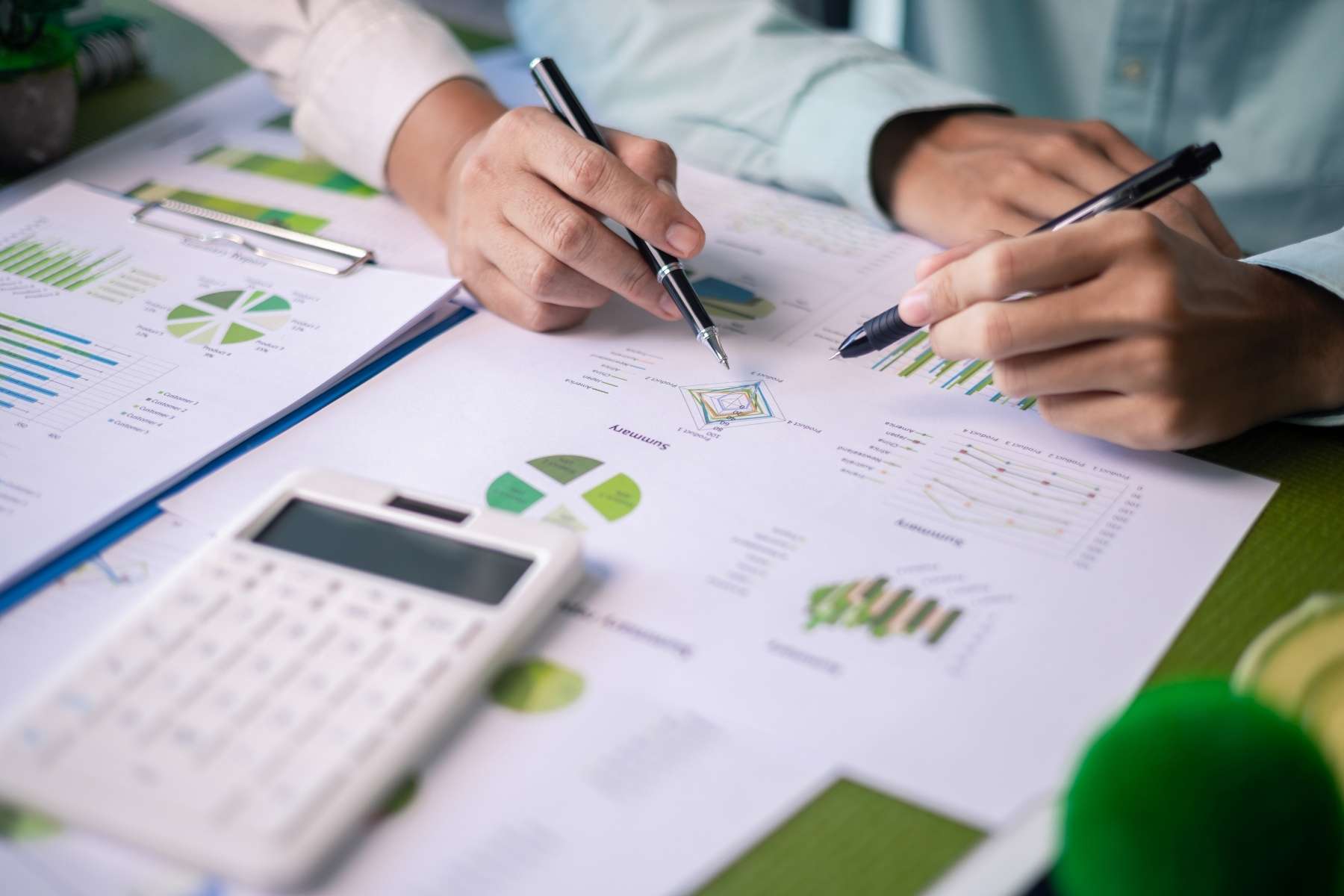 Nahaufnahme eines Tisches, an dem 2 Personen vor Dokumenten sitzen, die sich mit Umweltfaktoren beschäftigen als Sinnbild für kreislauffähige Büros.