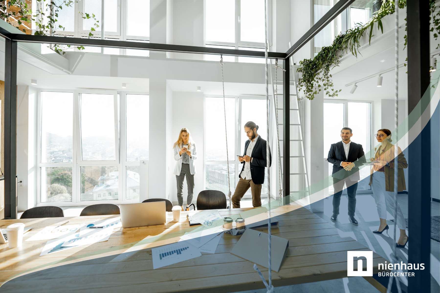 Vier Mitarbeiter stehen in einem hellen Büro mit großer Glasfront, hohen Decken und modernem Holztisch im Vordergrund,