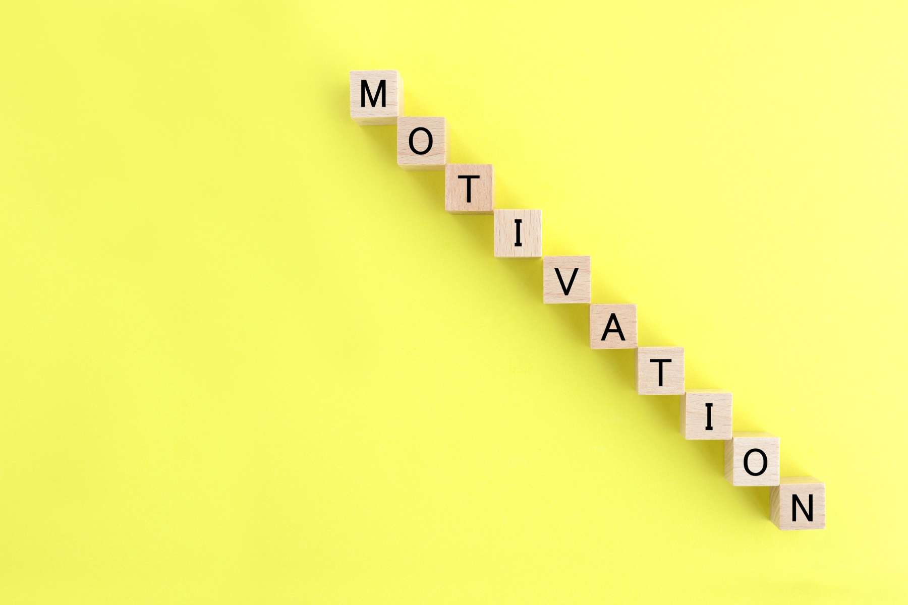 Das Wort Motivation ist aus einzelnen Bausteinen mit Buchstaben drauf als Treppe geformt und liegt auf einem hellgelben Hintergrund.