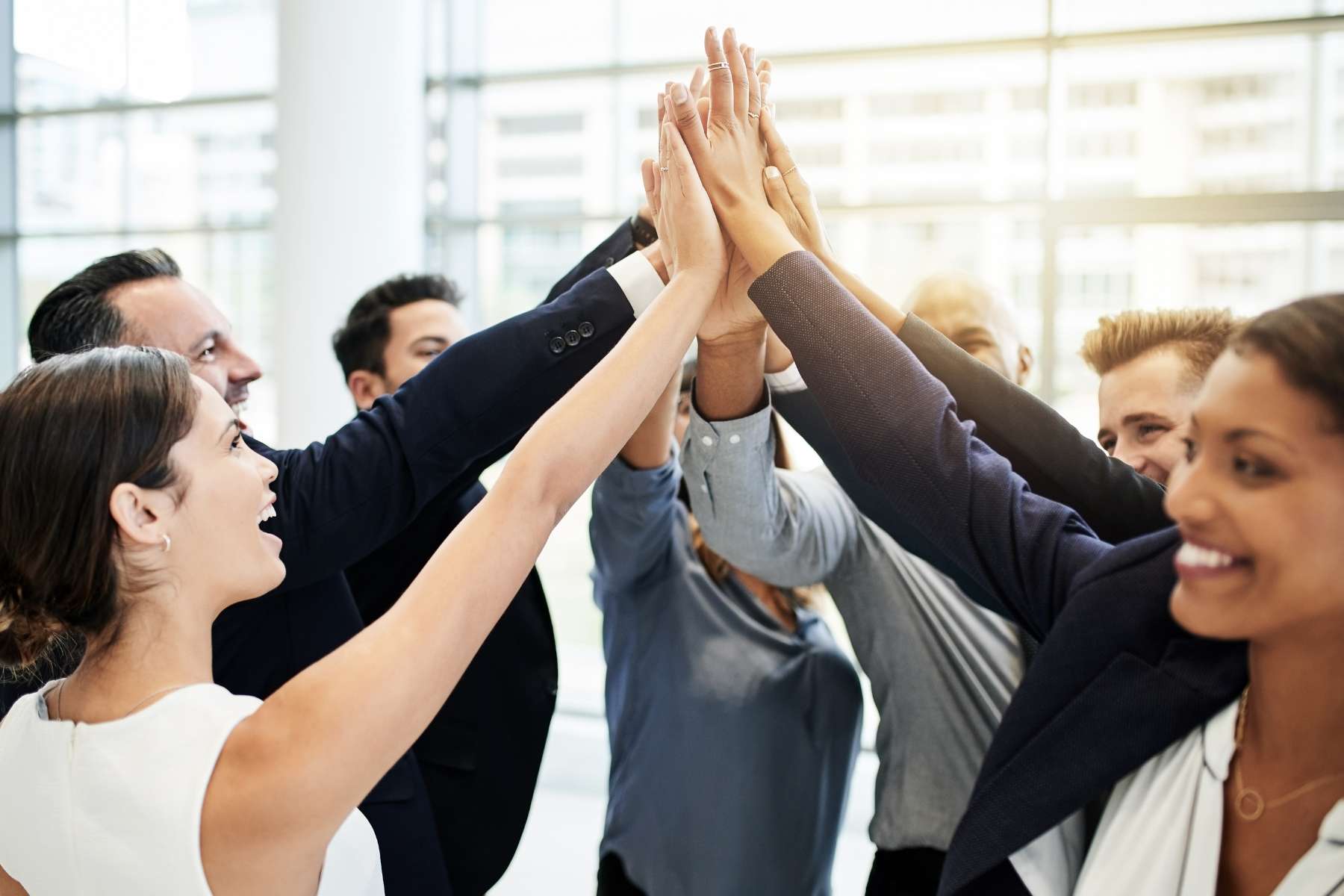 Gutgelaunte männliche und weibliche Büroangestellte bilden einen Kreis und schlagen in der Mitte mit den Händen zu einem High-five zusammen.