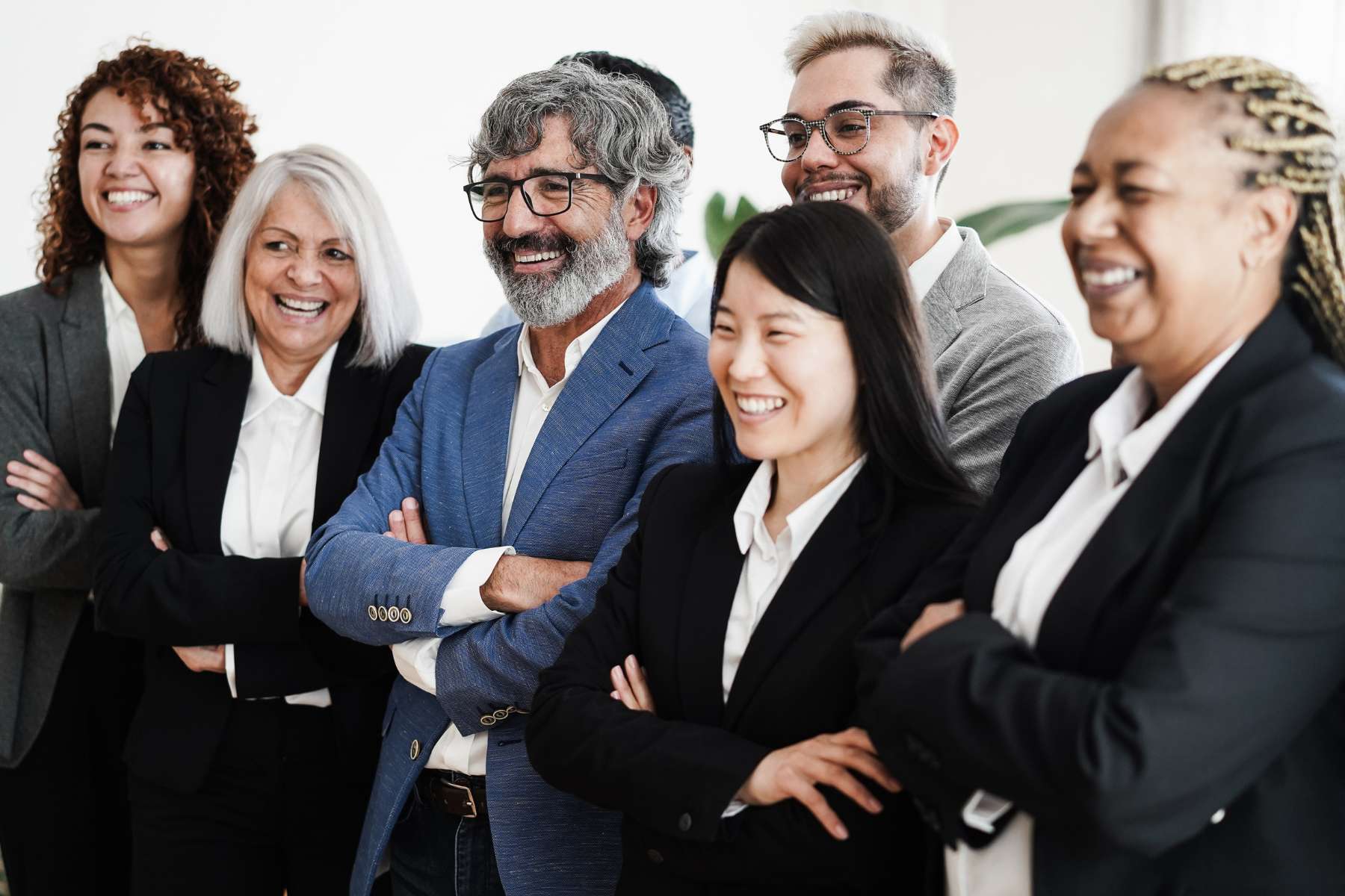 Eine Gruppe diverser Geschäftsführerinnen und Geschäftsführer in Hosenanzügen steht lachend und mit verschränkten Armen nebeneinander.
