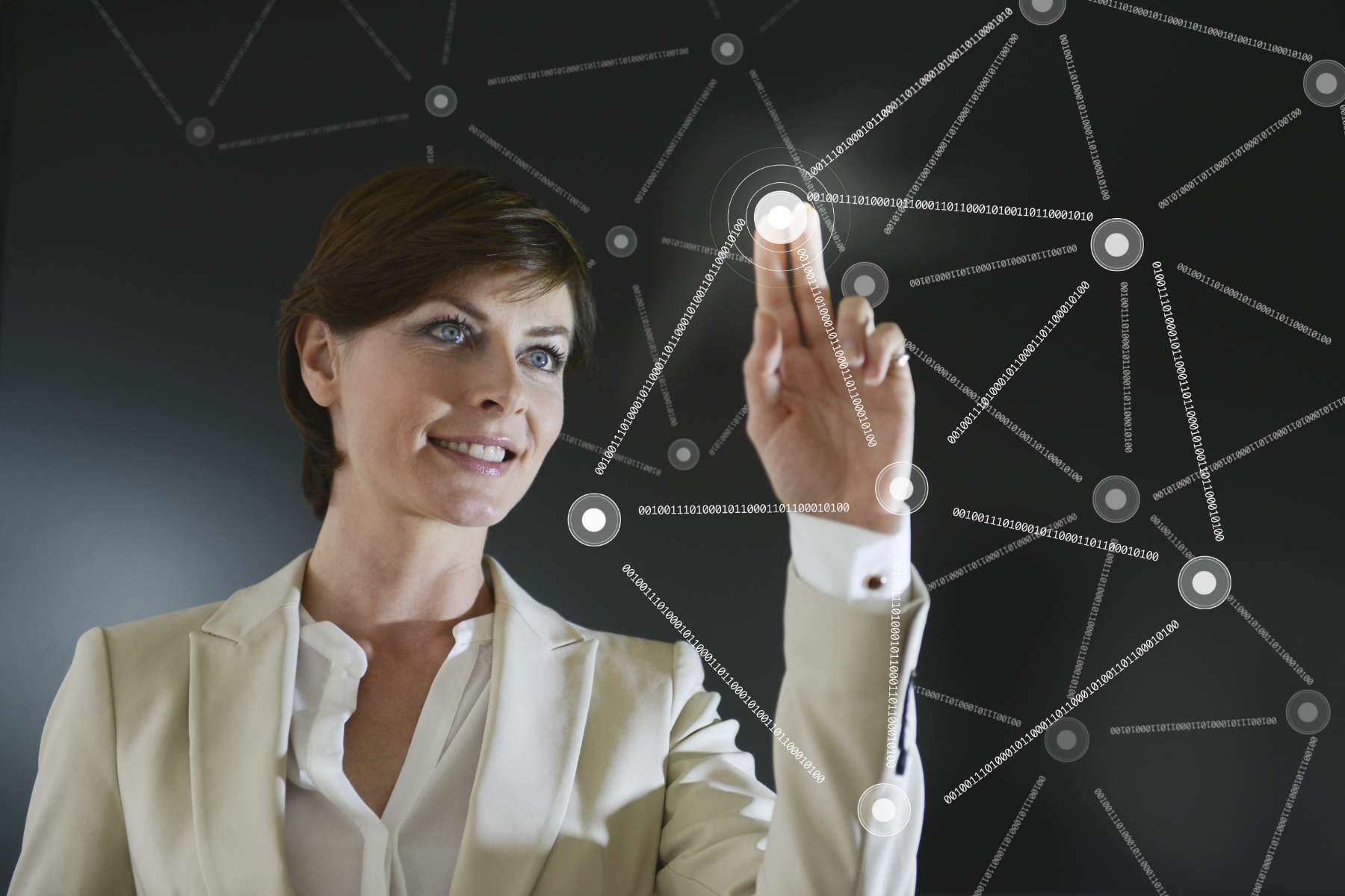 Eine junge weibliche Führungskraft in hellem Hosenanzug steht lächelnd vor einem digitalen Schaubild und arbeitet daran.