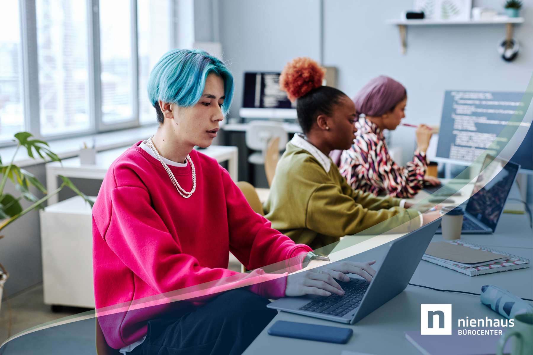 Ein junger Mann und zwei junge Frauen der Gen Z sitzen im Büro an Schreibtischen und arbeiten konzentriert an Laptops und Monitoren.