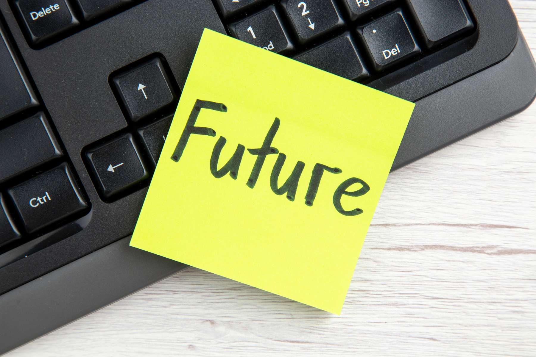 Ein gelber Post-it mit dem Wort Future haftet an einer schwarzen Tastatur, die auf einem Holztisch liegt.