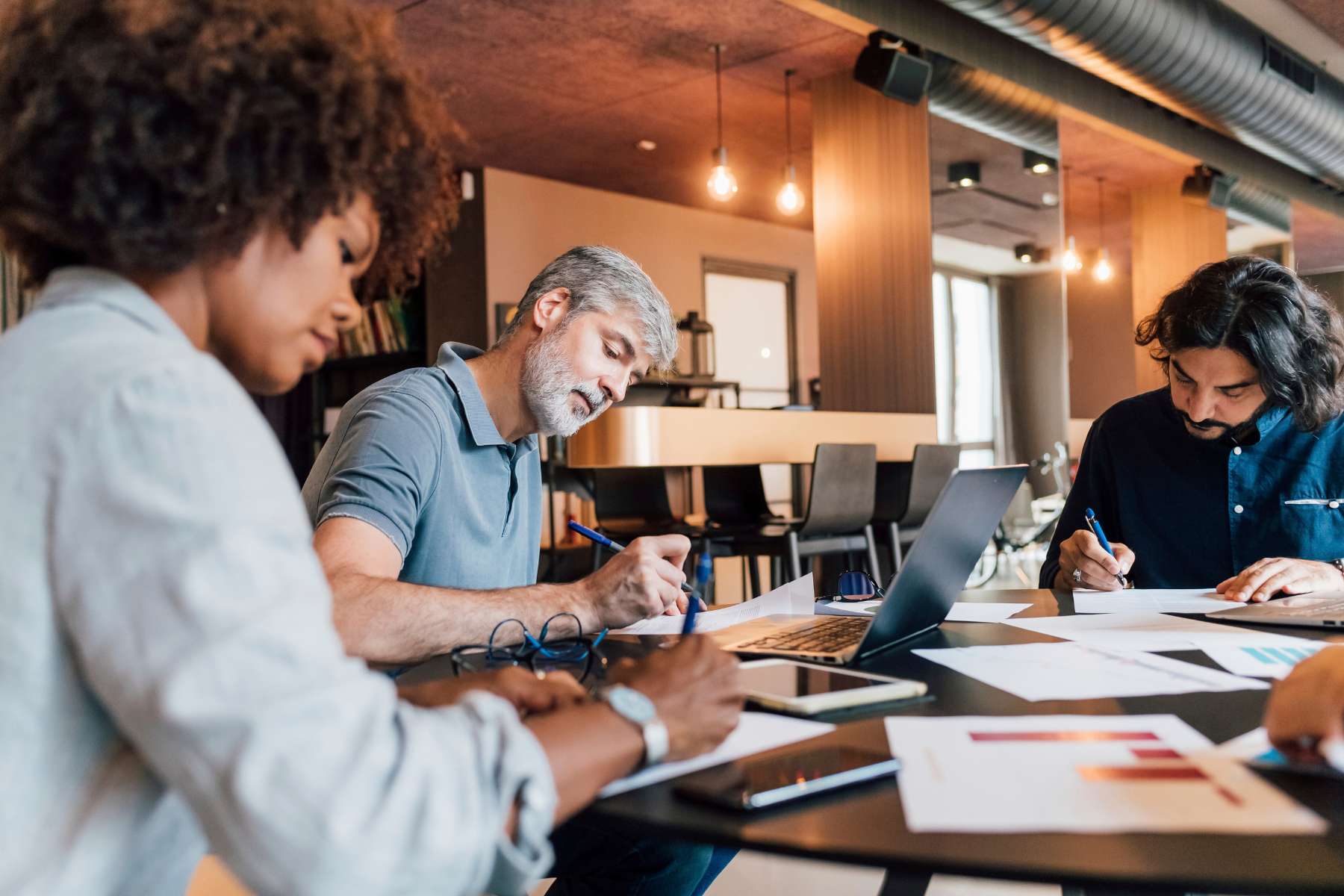 Drei Angestellte sitzen an einem dunklen Schreibtisch und bearbeiten konzentriert ein Projekt, als Beispiel für funktionierende Calm Technology im Büro.