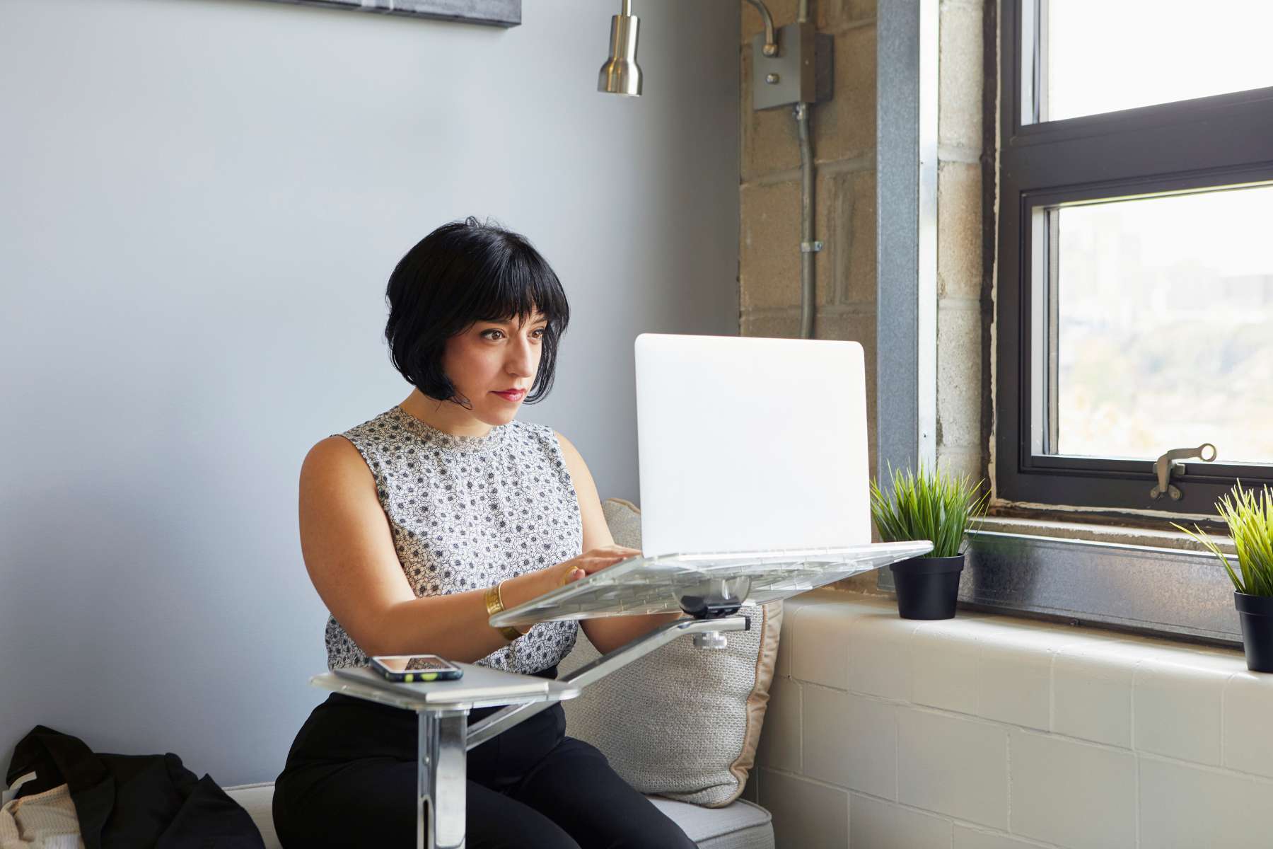 Dunkelhaarige Frau arbeitet an einem Laptop, der auf einer erhöhten Laptophalterung, einem Gadget für das Home-Office 2 Go, liegt.