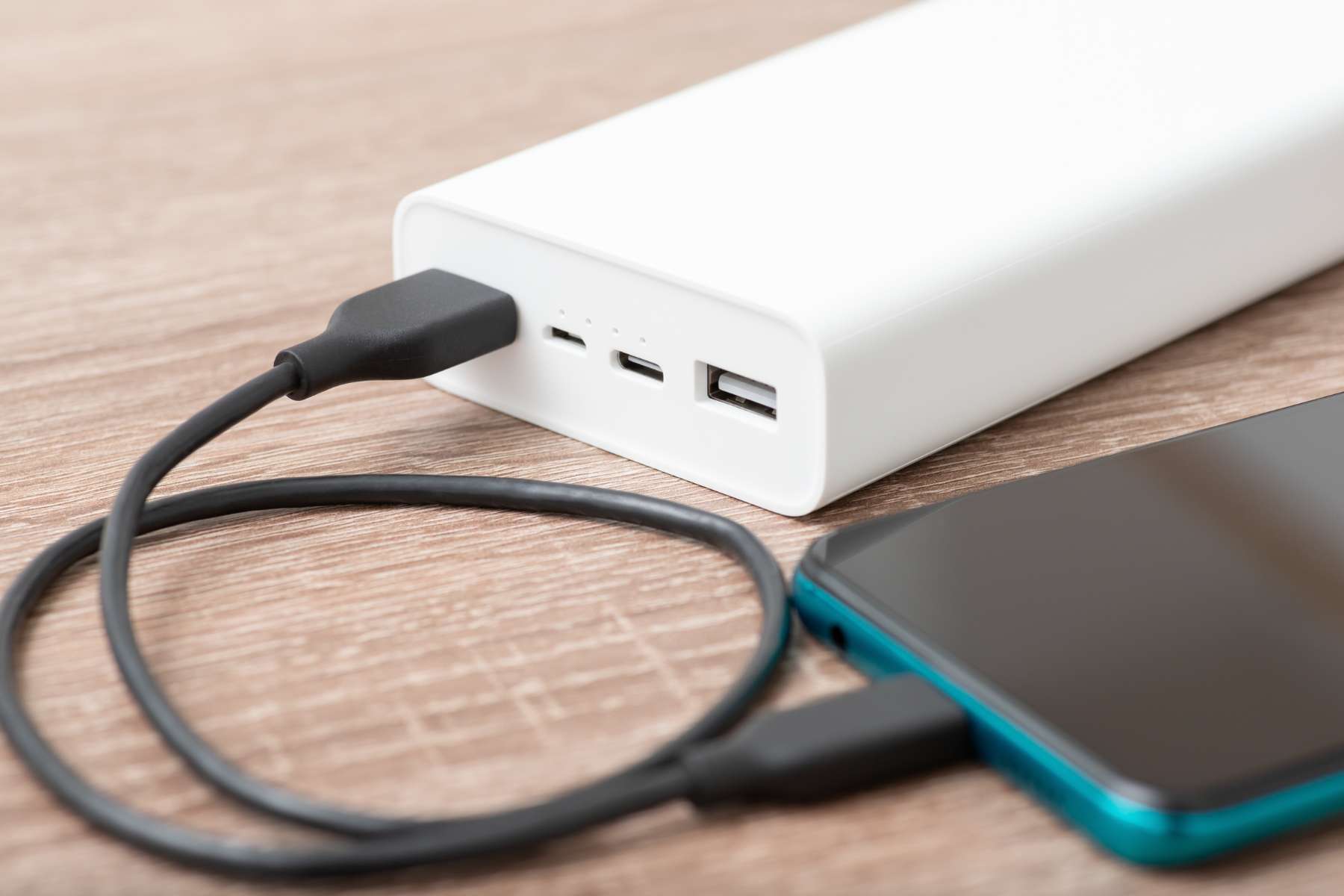 Nahaufnahme eines Handys, das an eine weiße Powerbank angeschlossen ist als Gadget für das Home-Office to Go.