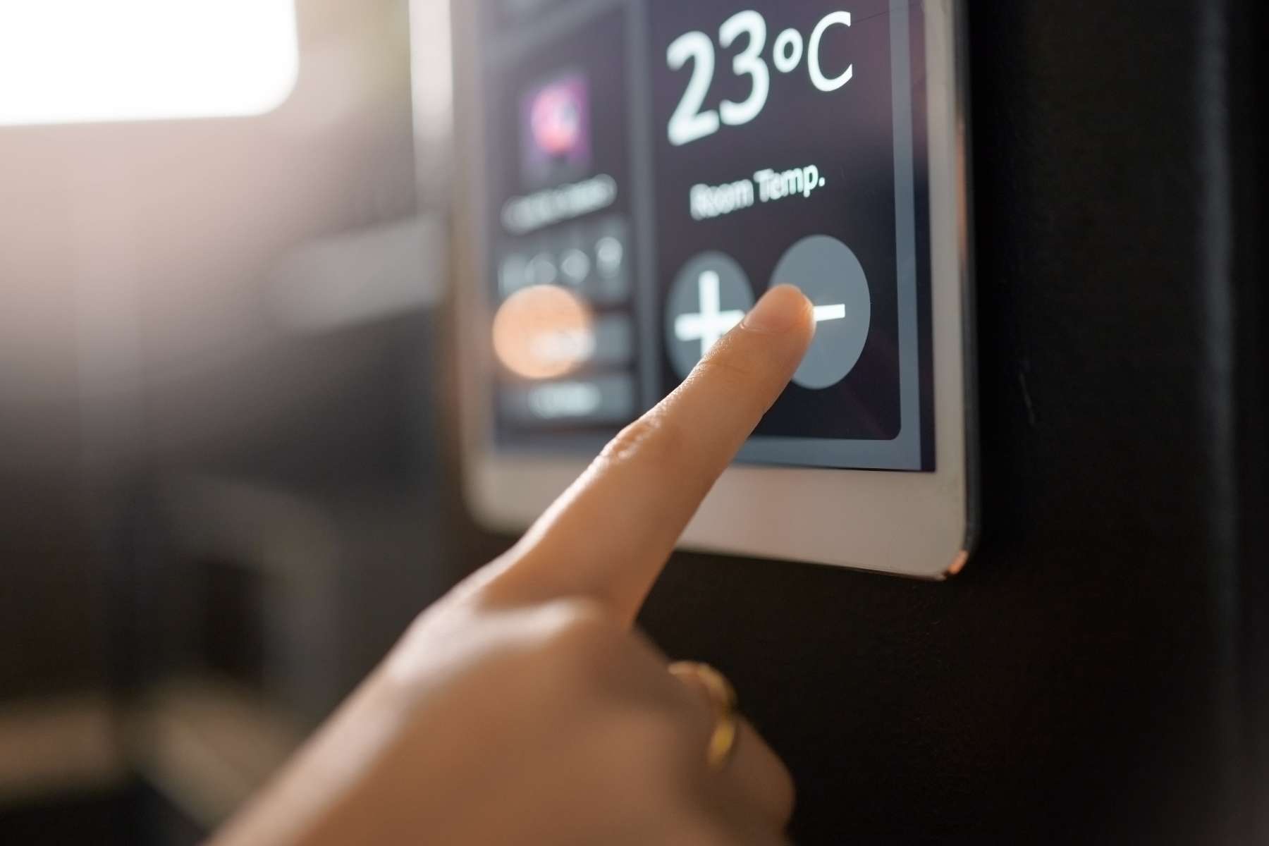 Nahaufnahme einer Hand, die ein elektrisches Thermometer einstellt, das momentan 23 Grad Raumtemperatur anzeigt,
