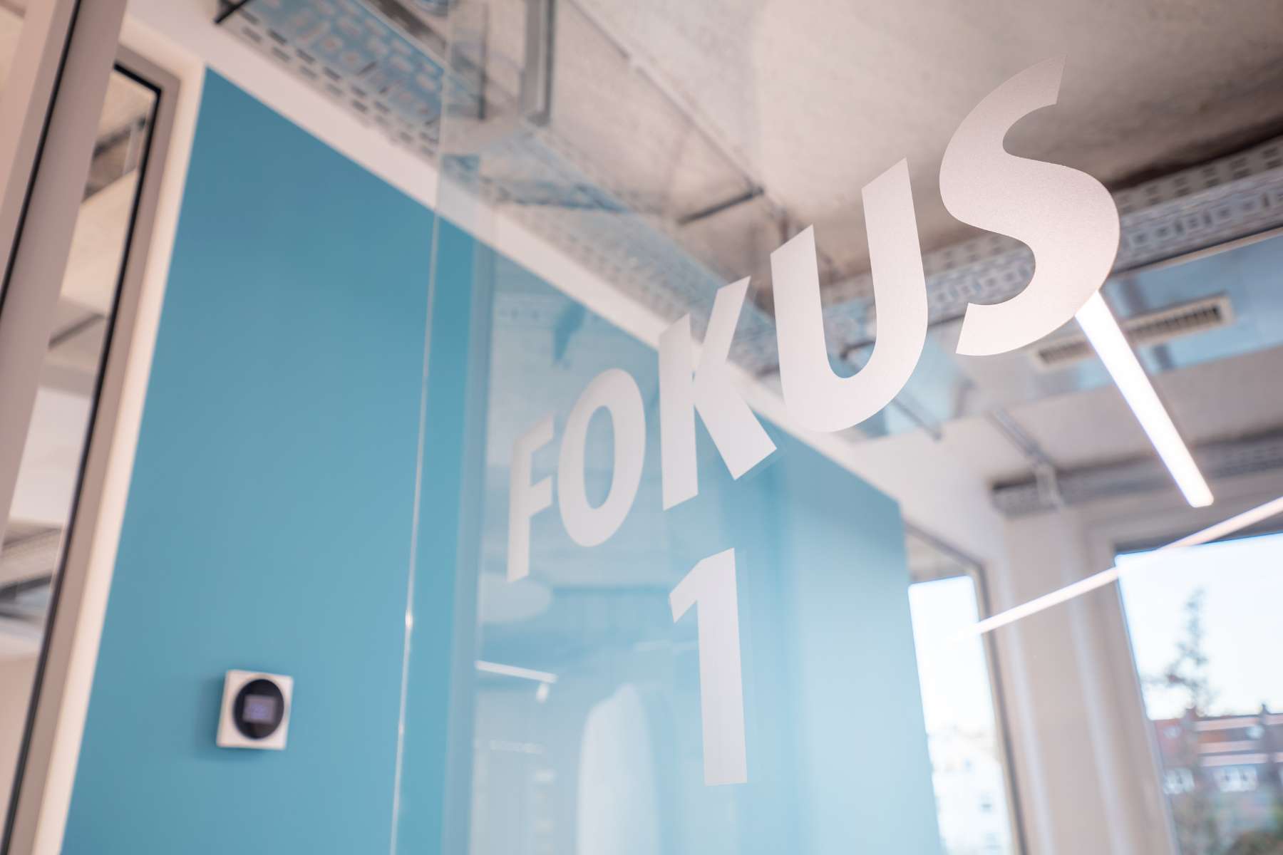 Nahaufnahme einer Bürotür aus Glas mit einer Folierung "Fokus 1".