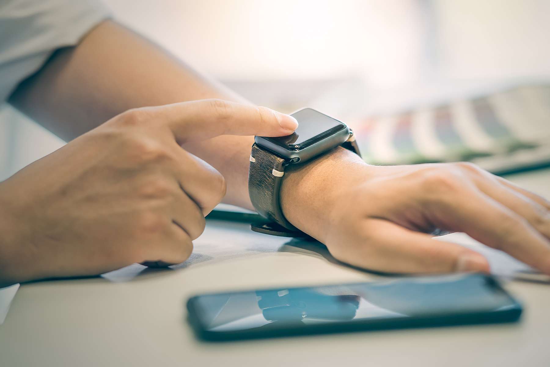 Männlicher Mitarbeiter hat ein Handy neben sich liegen und bedient gerade seine Smartwatch.