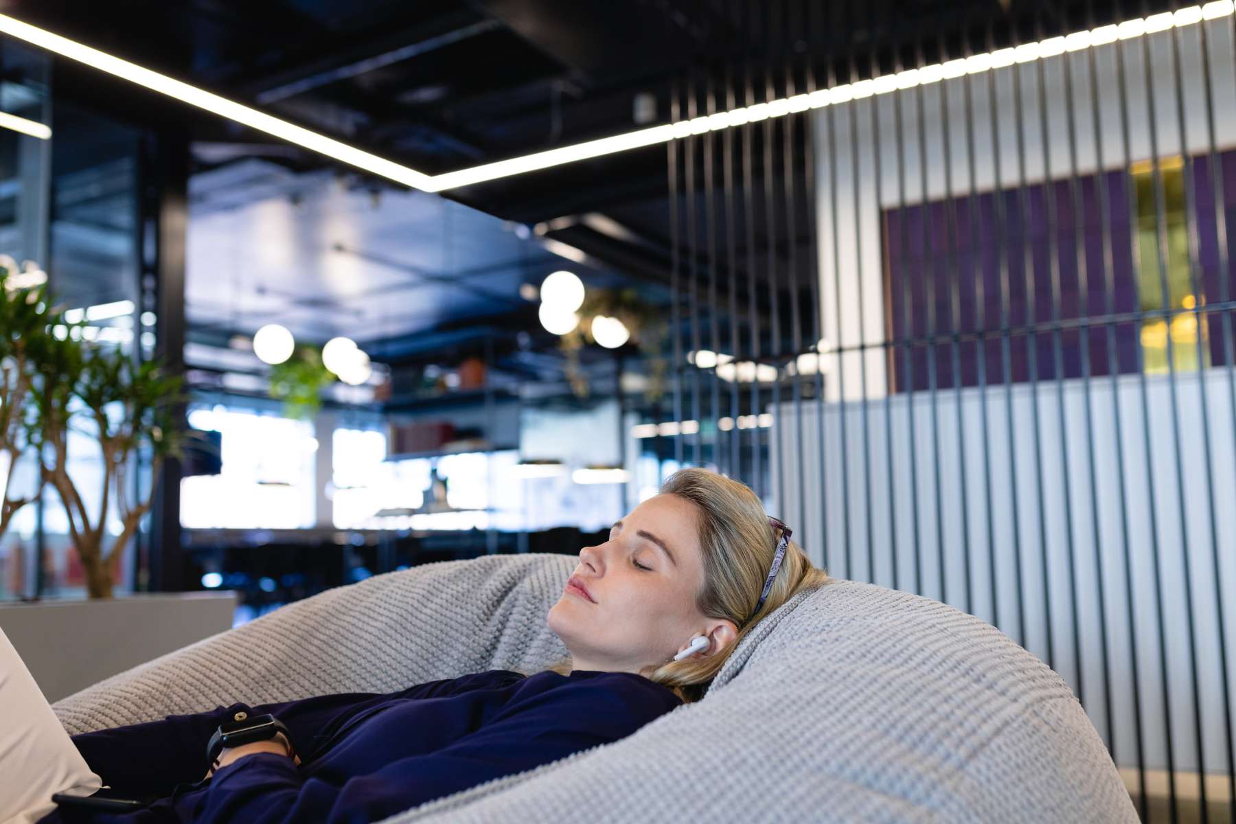Eine junge Angestellte liegt mit Kopfhörern in einem Sitzsack im Office und entspannt sich im Kontext von Wellbeing im Büro.