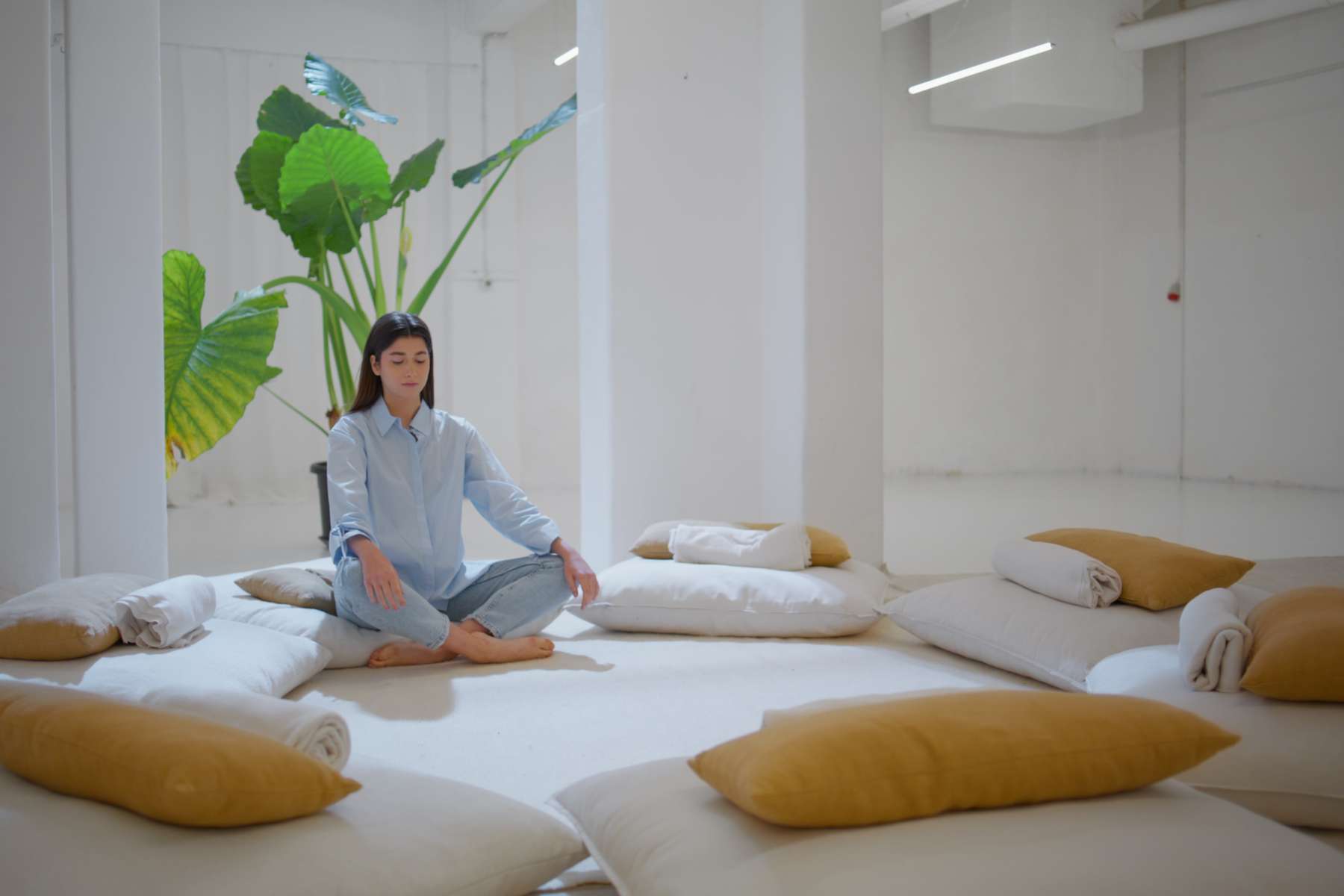 Junge Frau sitzt im Schneidersitz in einem Meditationsraum im Kontext Wellbeing im Büro.
