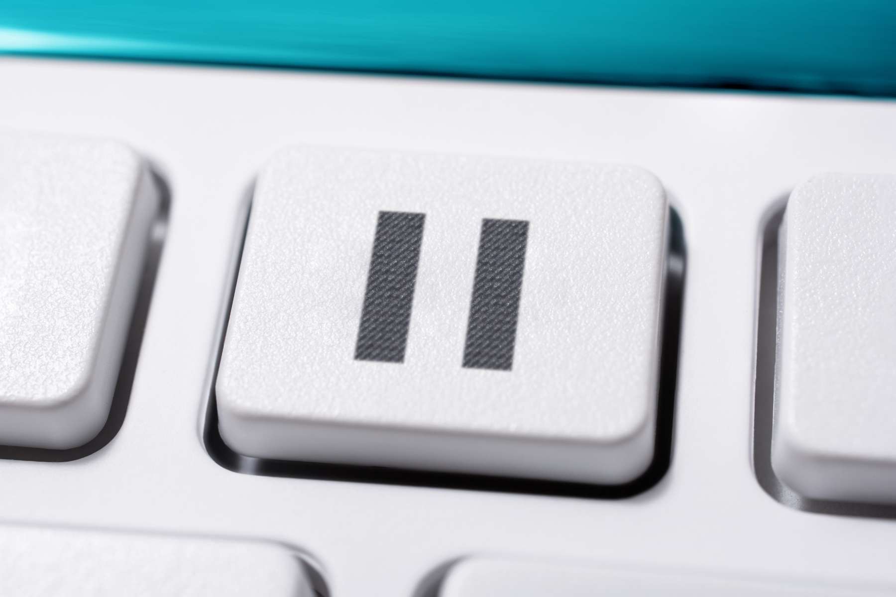 Nahaufnahme einer weißen Tastatur mit Fokus auf eine Taste mit einem Pause-Zeichen als Symbol für Wellbeing im Büro.
